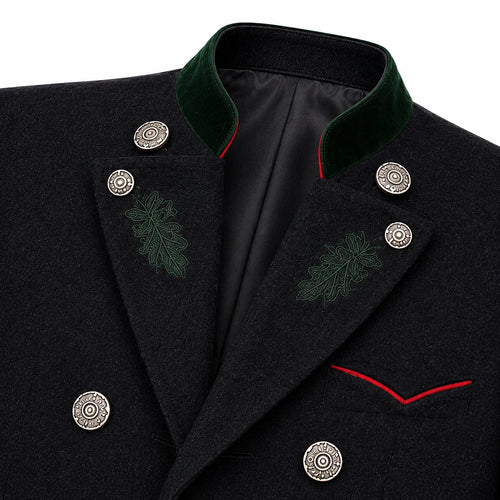 Close-up of a dark wool coat with a green velvet peak collar, silver decorative buttons, green embroidered leaf motifs on the lapels, and red piping detail.
